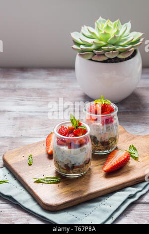 Joghurt Müsli Parfait mit Erdbeeren und Chia Samen. Gesunde Single-portion-Frühstück serviert im Glas Tassen auf Holzbrett mit grünen Serviette. Natu Stockfoto