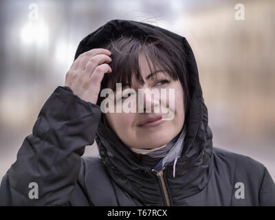 Porträt einer attraktiven Frau in einem schwarzen Jacke mit Kapuze vor dem Hintergrund der Straße Stockfoto