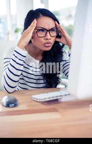 Asiatische Frau, die am Computer-Monitor mit Händen auf Kopf Stirnrunzeln Stockfoto