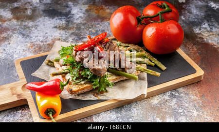 Gegrilltes Putenfleisch auf einem traditionellen chabbata mit Paprika, Tomaten und Kräutern auf einem Schneidebrett. Stockfoto