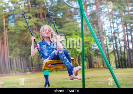 Hübsche kleine blonde Mädchen schwingen draußen auf dem Spielplatz Stockfoto