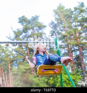 Hübsche kleine blonde Mädchen schwingen draußen auf dem Spielplatz Stockfoto