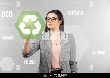 Junge Geschäftsfrau mit Recycling Symbol auf grauem Hintergrund Stockfoto