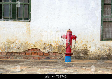 Eine alte rote Hydrant in einer gepflasterten Straße gegen eine gerissene Wand der kolonialen Stadt Villa de Leyva, in den Anden von zentraler Colo Stockfoto