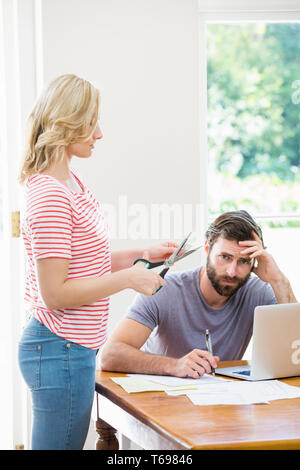 Frauenbeschneidung eine Kreditkarte während angespannten Mann mit Rechnungen, die am Tisch sitzen Stockfoto