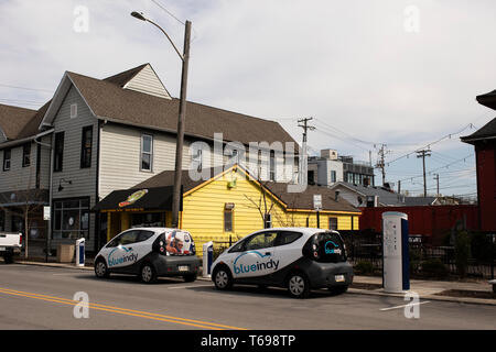 Blue Indy Elektroautos, die an einer Ladestation an der Broad Ripple Avenue in Indianapolis, Indiana, USA aufgeladen werden. Stockfoto