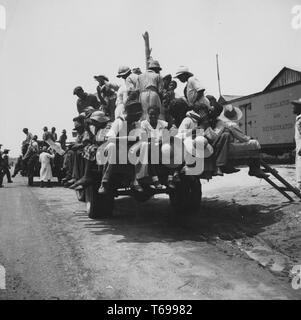 Schwarz-weiß Fotografie afroamerikanische Männer und Frauen boarding und saß auf Tieflader auf dem Weg zu ihrem Job als Landarbeiter auf einem Pfirsich Plantage in Muscella, Georgia, USA; mit einem Vordergrund Blick auf vier Personen sitzen auf der Rückseite des Staplers, darunter ein Mann mit einem kleinen Sonnenhut, eine lächelnde Frau mit einem großen Strohhut, und ein Mann, eine Frau; durch Dorthea Lange unter der Förderung der Farm Security Administration der Vereinigten Staaten, 1936 fotografiert. Von der New York Public Library. () Stockfoto
