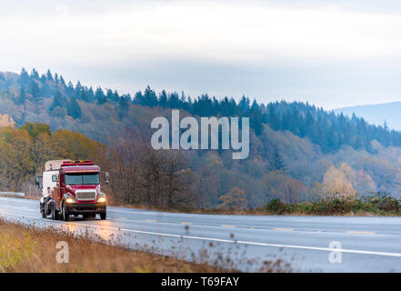 Dunkelrot Industrial Grade schweren Big Rig abschleppen Semi Truck tow hitched gebrochen Tag cab Semi Truck Traktor auf die Wicklung feuchten regnerischen Herbst Straße in t Stockfoto