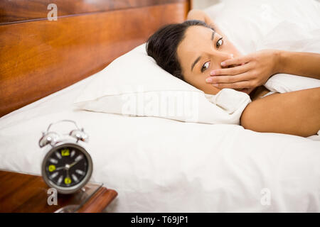 Brünette im Bett, Blick auf den Wecker auf dem Tisch Stockfoto