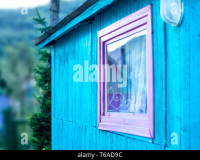 Minimalistisches Design Konzept: Vivid Lila Fensterrahmen, ein Licht auf blauen Wand der hölzernen Planken. Berg Reflexion in Glas, weißem Vorhang. Dachkehlen Stockfoto