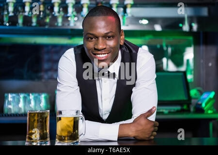 Barkeeper stützte sich auf Bartheke mit zwei Gläsern Bier vor ihm Stockfoto