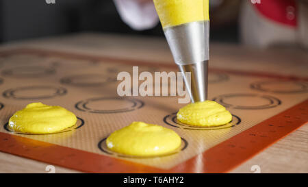 Konditor gießt Teig aus gebäckbeutel auf Schablone Silikon Matte auf dem Tisch. Kochen Makronen, close-up. selektive Fokus Stockfoto