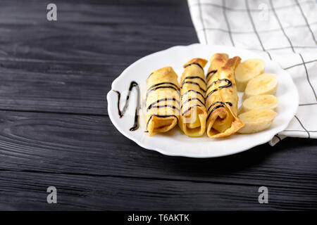 Pfannkuchen mit Banane mit Schokolade Sirup auf hölzernen Hintergrund eingerichtet. Ansicht von oben mit der Kopie. Stockfoto