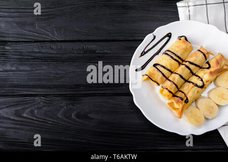 Pfannkuchen mit Banane mit Schokolade Sirup auf hölzernen Hintergrund eingerichtet. Ansicht von oben mit der Kopie. Stockfoto