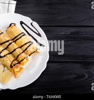 Pfannkuchen mit Banane mit Schokolade Sirup auf hölzernen Hintergrund eingerichtet. Ansicht von oben. Stockfoto