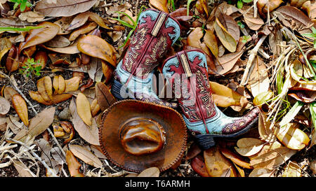 Teal und braune Cowboystiefel und Hut Festlegung auf einem Bett von Blättern Stockfoto