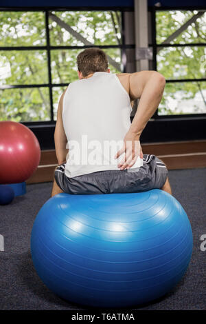 Rückansicht des Menschen seinen Rücken sitzen auf Fitness Ball berühren Stockfoto