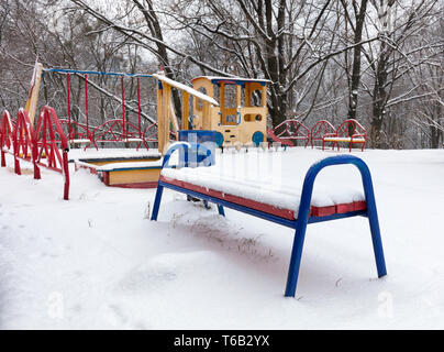 Schnee bedeckt die Bank und der bunten Kinderspielplatz im Innenhof des Winter Park Stockfoto