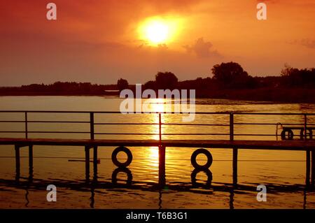 Seite, die Silhouette der Holzbrücke, Pier mit zwei Reifen auf der Seite bei Sonnenuntergang, Sonnenaufgang im Sommer, Feder Stockfoto