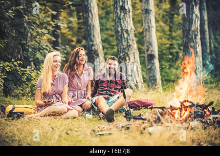 Gerne Freunde genießen Sie am Abend im Freien. Junger Mann und zwei Frauen sitzen am Lagerfeuer. Freunde Camping in der Wildnis Stockfoto