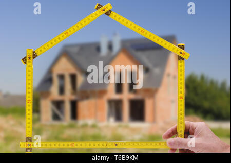 Shell von Haus im Bau mit Zollstock in der Hand von Real estate agent Stockfoto