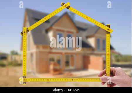 Shell von Haus im Bau mit Zollstock in der Hand von Real estate agent Stockfoto