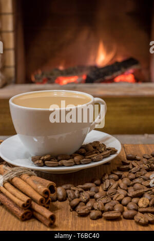Home Sweet Home. Szene in der Nähe der gemütlichen Kamin in der Grafschaft Haus mit Tasse Kaffee Milch, Kaffee Bohnen und Zimtstangen, senkrecht. Stockfoto