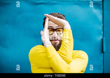 Porträt eines eleganten bärtigen Mann in gelb Pullover und Sonnenbrille auf dem blauen Hintergrund Stockfoto