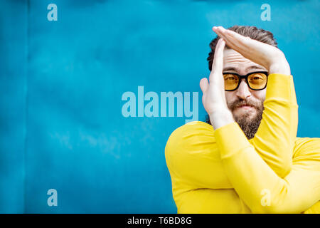 Porträt eines eleganten bärtigen Mann in gelb Pullover und Sonnenbrille auf dem blauen Hintergrund Stockfoto