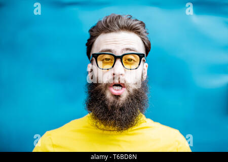 Nahaufnahme Porträt eines verwirrten bärtigen Mann in gelb Pullover und Sonnenbrille auf dem blauen Hintergrund Stockfoto