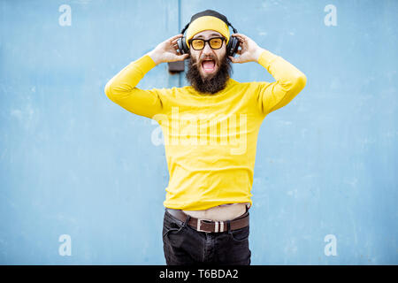 Porträt eines eleganten bärtigen Mann in gelber Kleidung genießen Sie Musik mit Kopfhörer auf dem blauen Hintergrund Stockfoto