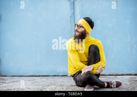 Porträt einer stilvollen Mann in gelb Pullover sitzen auf der blauen Wand Hintergrund im Freien Stockfoto