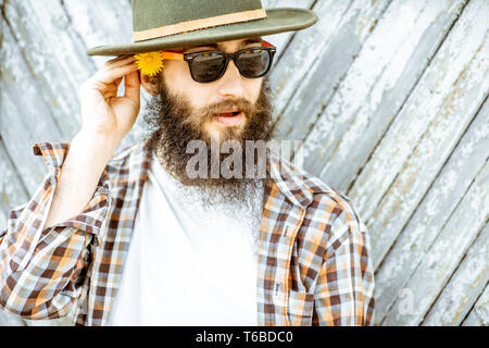 Porträt einer stilvollen Mann mit Blume und Hut auf dem hölzernen Tor Hintergrund im Freien Stockfoto