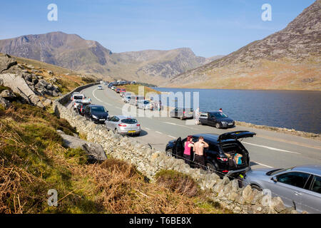 Autos auf der Straße und Bürgersteig entlang einer 5-Straße in Ogwen Valley am langen Osterwochenende geparkt in Snowdonia National Park. Ogwen North Wales UK Großbritannien Stockfoto