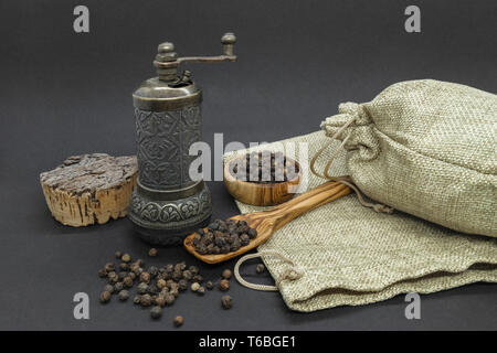 Zusammensetzung aus Metall Handbuch vintage Pfeffermühle, schwarzer Pfeffer Körner, olivenholz Schüssel und Löffel und jutetaschen auf schwarzem Hintergrund Stockfoto