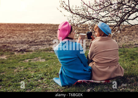 Gerne ältere Mutter und ihrer Tochter sitzen und Kaffee trinken von Spring River bei Sonnenuntergang. Muttertag Konzept. Die Werte der Familie Stockfoto