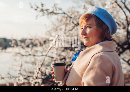 Ältere Frau trinkt Kaffee und entspannen Sie im Frühling Garten bei Sonnenuntergang. Muttertag Konzept Stockfoto