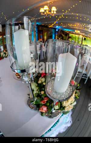 Tischdekoration zur Hochzeit. Kerzenständer mit Kerzen und Blumenstrauß auf Hochzeit Tisch mit weißer Tischdecke. Schuss mit Fisch Stockfoto