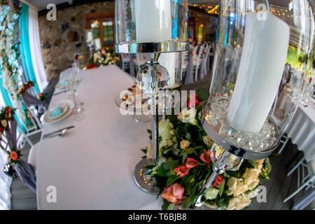 Tischdekoration zur Hochzeit. Kerzenständer mit Kerzen und Blumenstrauß auf Hochzeit Tisch mit weißer Tischdecke. Schuss mit Fisch Stockfoto