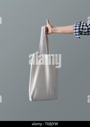 Blank Canvas Bag Eco Produkt eine Frau, die Tote hält eine wiederverwendbare weiß Shopping Bag gegen eine graue Wand Hintergrund Stockfoto