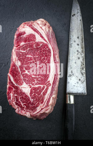 Raw trockenen Jahren Rib Eye Steak mit Messer auf einem Schiefer Stockfoto