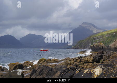 Kleine rote Fischerboot auf dem Loch Scavaig, dominiert von der Cullin Mountains auf einem Stimmungsvollen Herbsttag. Elgol, Isle of Skye, Schottland, Großbritannien. Stockfoto