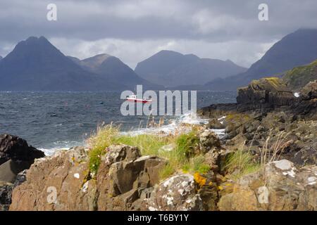 Kleine rote Fischerboot auf dem Loch Scavaig, dominiert von der Cullin Mountains auf einem Stimmungsvollen Herbsttag. Elgol, Isle of Skye, Schottland, Großbritannien. Stockfoto