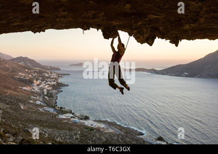 Weibliche Kletterer auf die anspruchsvolle Strecke, die in der Höhle bei Sonnenuntergang, Kalymnos, Griechenland Stockfoto