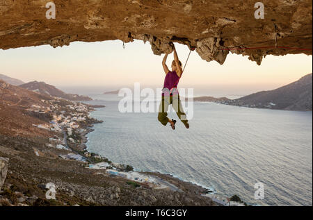 Weibliche Kletterer auf die anspruchsvolle Strecke, die in der Höhle bei Sonnenuntergang, Kalymnos, Griechenland Stockfoto