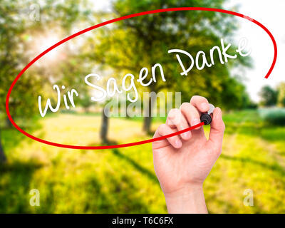 Mann Hand schreiben Wir sagen Danke (Wir sagen Vielen Dank, dass Sie sich in Deutscher Sprache) mit schwarzem Marker auf visuelle Bildschirm Stockfoto
