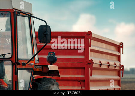 Alten roten landwirtschaftlichen Traktor mit Anhänger auf Schmutz Landstraße im Frühjahr am Nachmittag Stockfoto