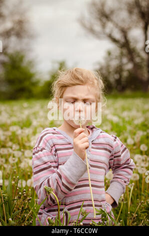 Adorable blonde Mädchen bläst Löwenzahn Blume in einer schönen Wiese Stockfoto