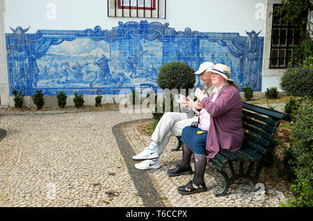 Senioren Touristen sitzen auf der Bank durch historische Darstellung von Seige Von Lissabon 1147 in blauen Wandfliesen Azulejos Alfama Lisboa PORTUGAL EU KATHY DEWITT Stockfoto