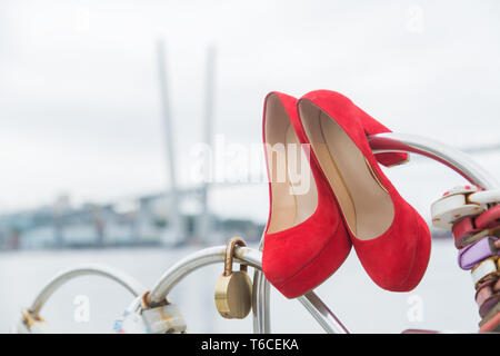 Rot luxus Schuhe hängt am Zaun mit Schlössern der Herzen gegen den Himmel Stockfoto